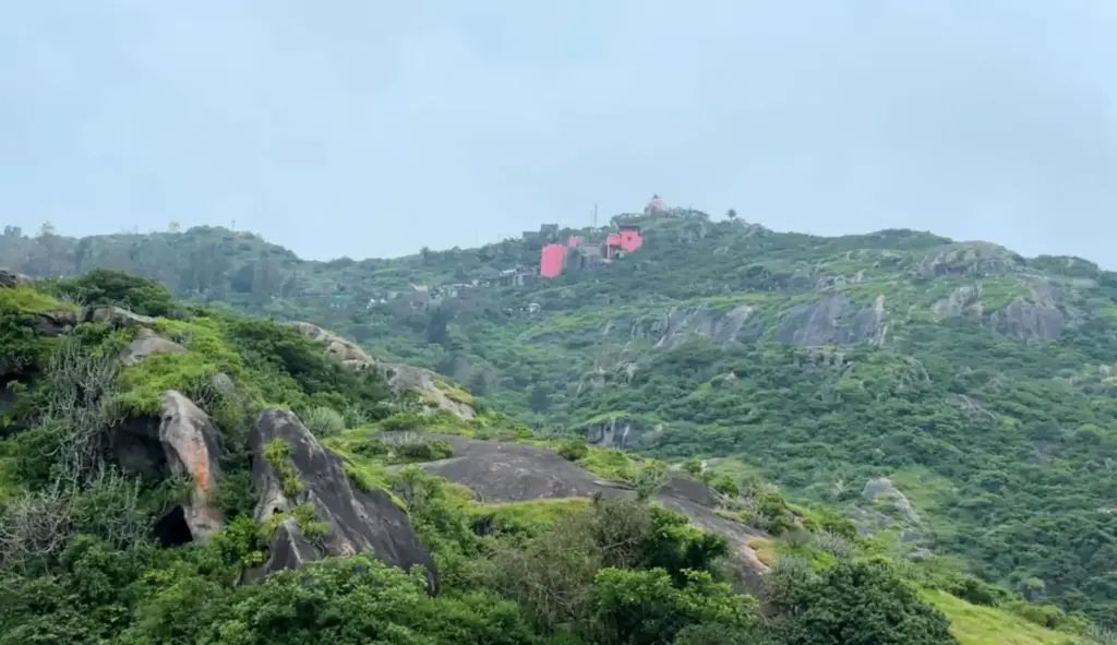 Distant view of Guru Shikhar hill surrounded by green landscape in Mount Abu